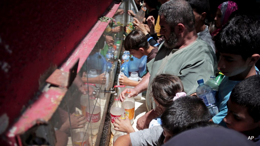 In this Monday, July 14, 2014 photo, displaced Palestinians fill empty bottles of water at the New Gaza Boys United Nations School, where dozens of families have sought refuge after fleeing their home in fear of Israeli airstrikes. Families sought shelter in the same U.N. school where they stayed during the previous two rounds of fighting. In all, 20 U.N. schools took in more than 17,000 displaced Gazans, many of them children, after Saturday's warnings by Israel that civilians must clear out of northern Gaza. (AP Photo/Khalil Hamra)