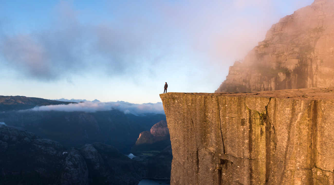 Human standing on the edge of a cliff on a misty morning.